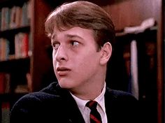 a young man wearing a suit and tie in front of a book shelf with books