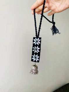 a hand holding a black and white necklace with bells on it's end,