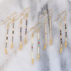 Edgy minimalism at its finest. These simple, long beaded stick earrings in a lean linear shape are just the right thing when you want a subtly cool accent. A tiny gold spike finishes the look with don't-mess-with-me edge. beaded gold-plated pin with tiny glass seed beads gold-plated stainless steel earwire hooks lead-free and nickel-free gold-plated spike charm plastic earring back 3 inches long packaged on a logo kraft card in a clear resealing bag Simple Bead Earrings, Long Beaded Earrings, Pebble Jewelry, Diy Earrings Easy, Homemade Bracelets, Stick Earrings, Beaded Earrings Tutorials, Beaded Earrings Diy, Plastic Earrings