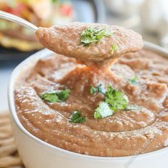 a spoon full of dip with cilantro and parsley on top in a white bowl