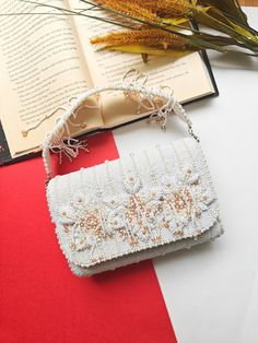 Unique Bridal Flap Bag with 3D Floral Design, Beaded Handle, Tassels & Fringes - Ivory Beaded Bridesmaid Clutch, One-of-a-Kind Wedding Purse Discover the epitome of elegance with this one-of-a-kind bridal flap bag, meticulously crafted to add a touch of sophistication to your wedding day ensemble. The exquisite 3D floral design is intricately adorned with white and beige beads, creating a stunning visual effect that exudes luxury. This bridal bag is not only perfect for brides but also makes an Bridal Clutch Bag, Bridesmaid Clutches, Bridal Purse, Clutch Bag Wedding, Floral Handbags, Bridal Bag, White Purse, Wedding Purse, Bridal Clutch