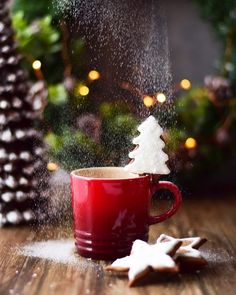 a cup of coffee and some cookies on a table with christmas lights in the background