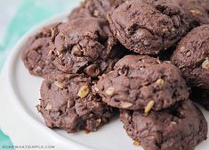 three chocolate cookies with pistachios are on a white and brown plate next to a striped tablecloth