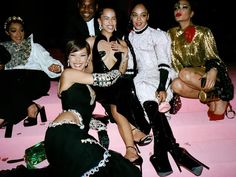 a group of women sitting on top of a pink floor next to each other wearing black and white outfits