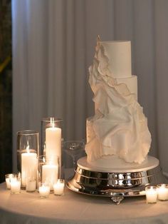 a white wedding cake sitting on top of a table surrounded by candles and votives