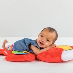 a baby laying on top of a red stuffed animal with his arms around it's head