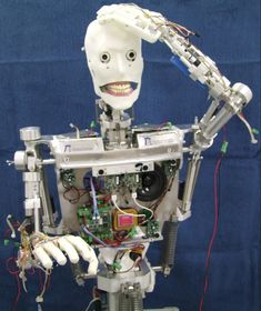 a robot that is standing in front of a blue wall with wires and wires attached to it