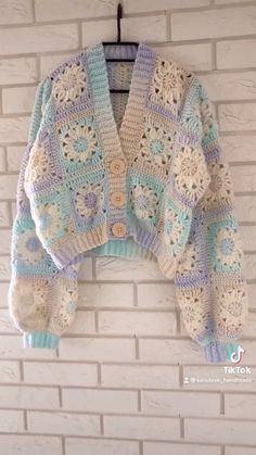 a crocheted sweater hanging on a brick wall next to a white brick wall