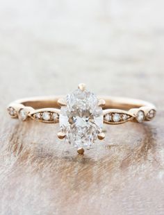 an oval shaped diamond ring on top of a wooden surface with diamonds around the band