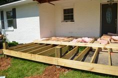 a house that is being built with some wood on the ground and grass in front of it