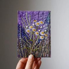 a hand holding up a piece of paper with daisies on it and purple background