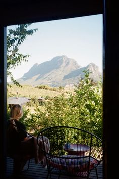 a woman sitting on top of a wooden deck next to a table with chairs around it