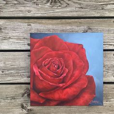 a painting of a red rose on a wooden surface