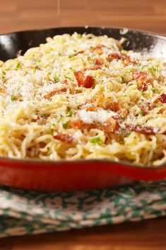 a pan filled with pasta and sauce on top of a wooden table next to a napkin