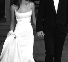 a bride and groom holding hands walking down the street in front of a building on their wedding day