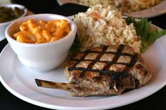 a white plate topped with steak and macaroni and cheese next to a bowl of cole slaw