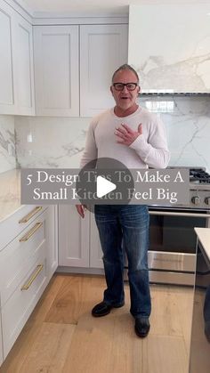 a man standing in the middle of a kitchen with white cabinets and marble counter tops