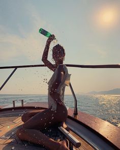 a woman sitting on the back of a boat drinking from a green bottle while splashing water