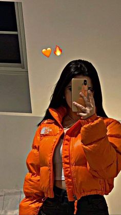 a woman in an orange puffer jacket taking a selfie with her cell phone