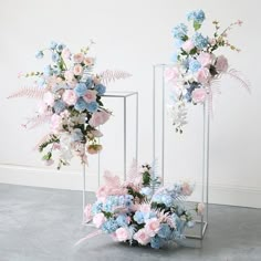 two vases with flowers and ferns in them on the floor next to each other