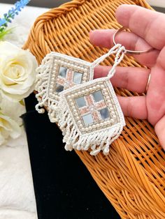 a hand holding a small white beaded pendant on a woven basket next to flowers