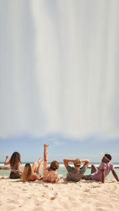 four people are sitting on the beach and one person is flying a kite in the air