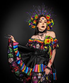 a woman in a colorful dress and headdress poses for the camera with her hands on her hips