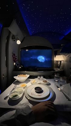 a person sitting at a table in front of a flat screen tv with food on it