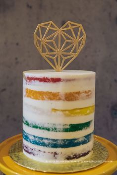 a multicolored cake with a gold heart decoration on top is sitting on a yellow plate