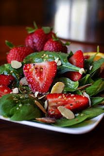 a salad with strawberries and spinach leaves on a white plate sitting on a wooden table