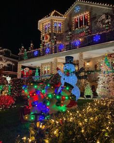 a house covered in christmas lights with snowmen and trees on the front lawns