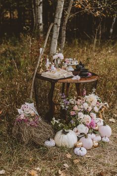 a table with flowers and other items on it in the woods next to some trees