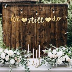 a table with white flowers and greenery is set up in front of a wooden wall