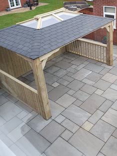 a wooden bench sitting on top of a patio next to a brick wall and green grass