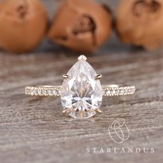 a pear shaped diamond ring sitting on top of a wooden table next to some nuts