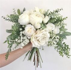 a bouquet of white roses and greenery in someone's hand on a white background