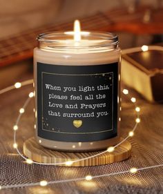 a candle with a quote on it sitting on a table next to a book and some string lights