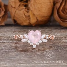 a pink heart shaped stone surrounded by white diamonds on top of a wooden table next to flowers