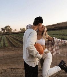 a man and woman kissing while holding pumpkins