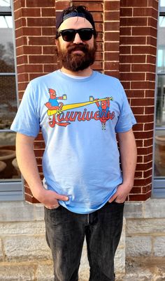 a man standing in front of a brick building wearing sunglasses and a blue shirt with the word kentucky on it