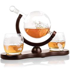 three glasses and a decanter are sitting on a stand with a globe in the middle