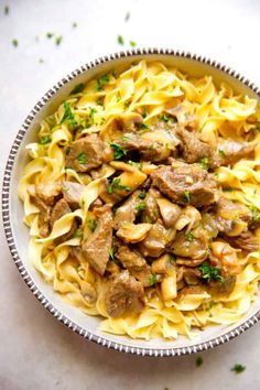 a bowl filled with pasta and meat on top of a white countertop next to parsley