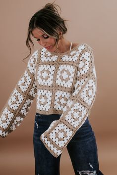 a woman wearing a sweater with crochet on the shoulders and sleeves, standing in front of a brown background