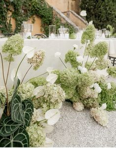 white flowers and greenery in front of a table set for an outdoor wedding reception