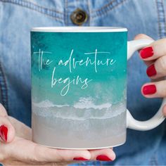 a woman holding a coffee mug with the words, the adventure begins written on it