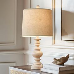 a lamp that is sitting on top of a dresser next to a book and a bird