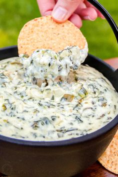 a tortilla chip being dipped into a bowl of spinach artichoke dip