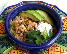 a blue bowl filled with beans and avocado on top of a colorful plate