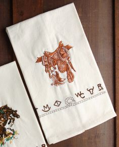 two embroidered tea towels with horses on them sitting on a wooden table next to each other