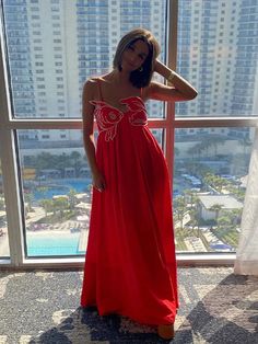 a woman standing in front of a window wearing a red dress